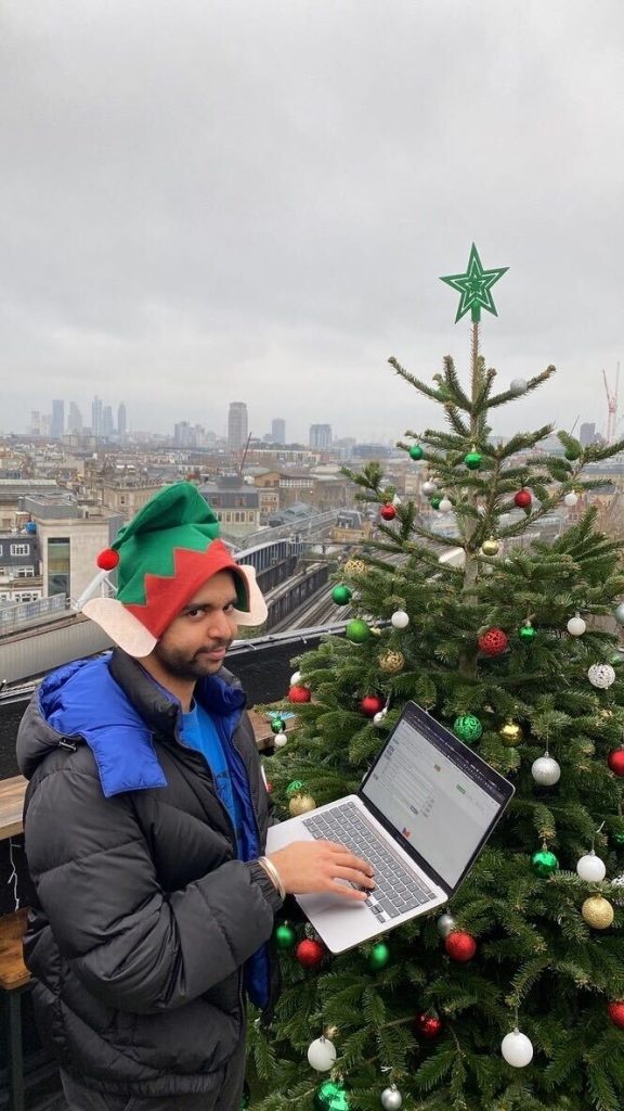 Mehul still working away on his laptop next to the Christmas tree on the top of the London Bridge rooftop bar. 