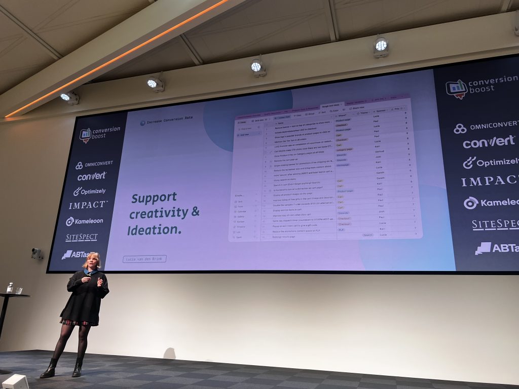 Lucia van den Brink stands on stage at Cboost, presenting to the audience with a slide behind her about supporting creativity and ideation.