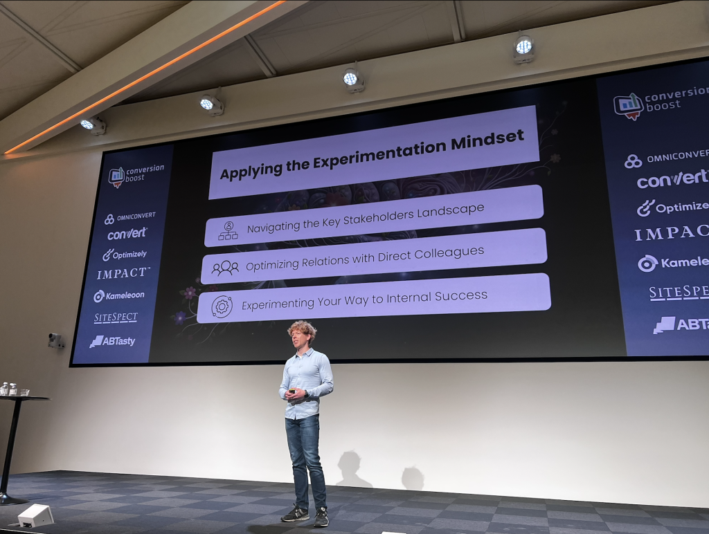 Ruben de Boer stands on stage at Cboost in front of a large screen displaying the slide titled "Applying the Experimentation mindset," delivering his presentation to the audience.