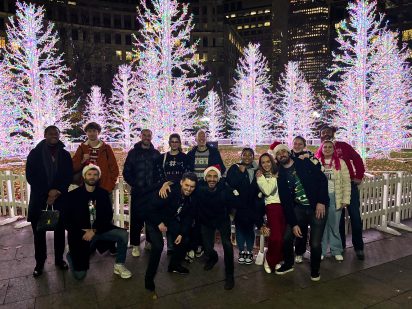 A group of Creative CX team members standing together outdoors at night, with christmas trees in the back
