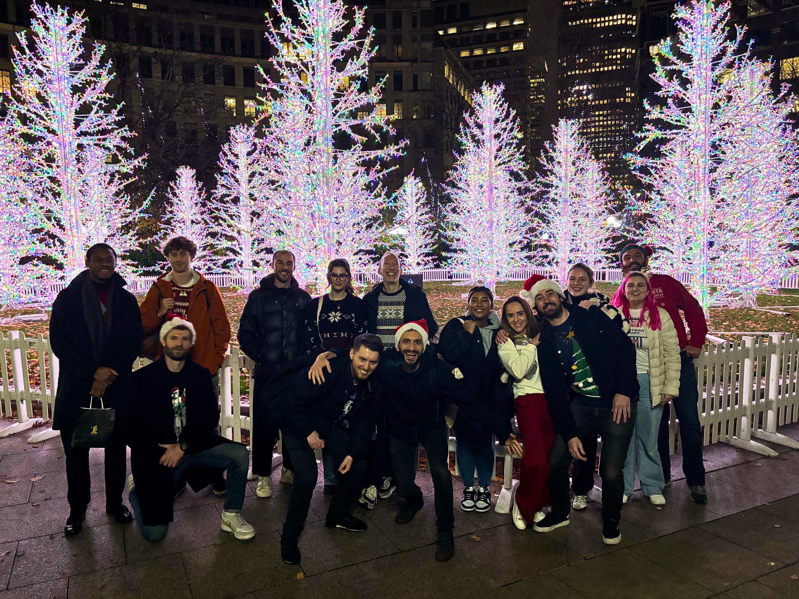 A group of Creative CX team members standing together outdoors at night, with christmas trees in the back