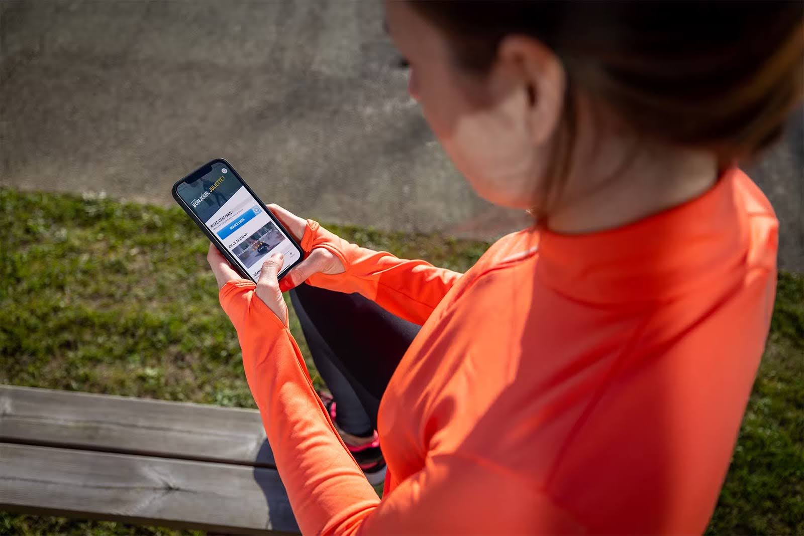 A person sitting outdoors using a smartphone, viewing a mobile website while wearing an orange athletic top
