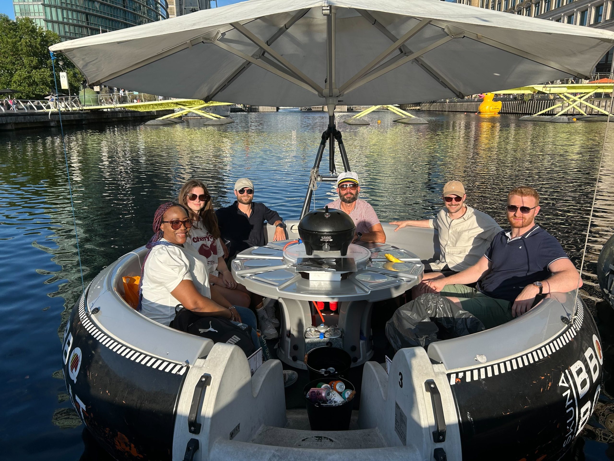 A group of Creative CX team members sitting together on a round boat with a barbecue set up in the centre.