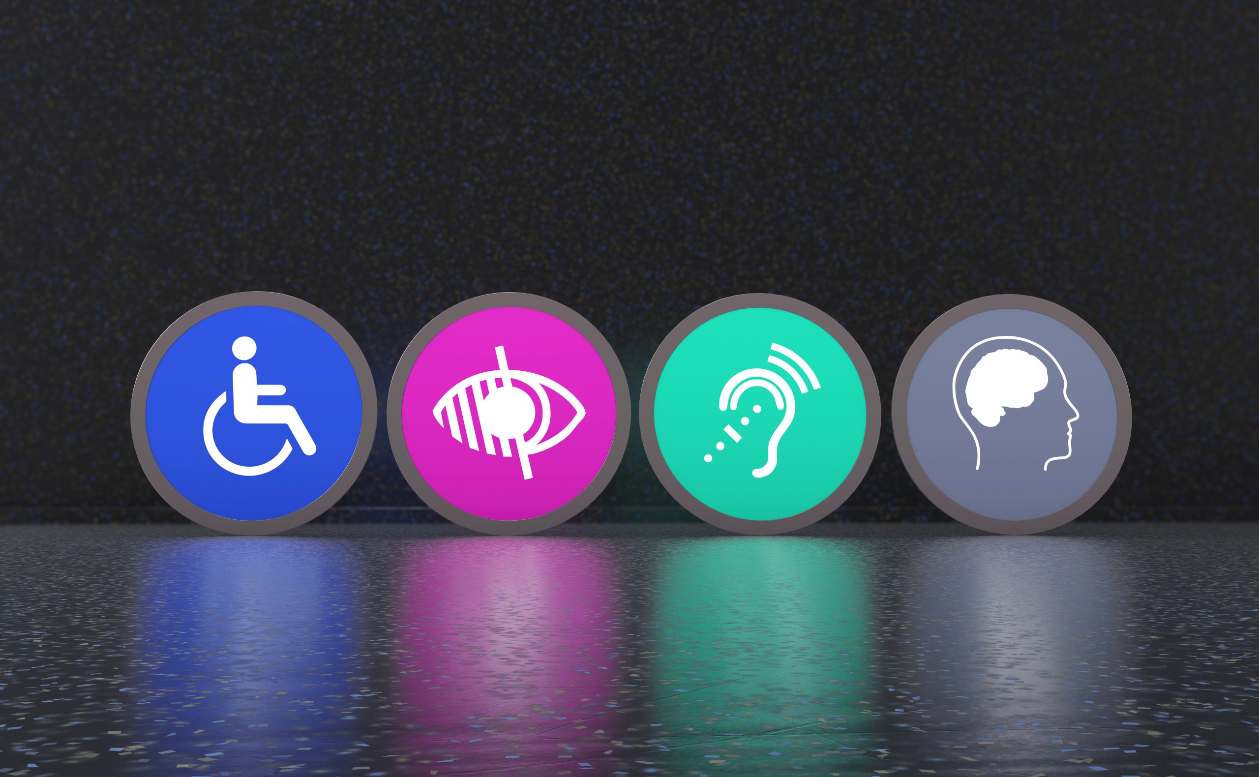 Four circular accessibility icons displayed side by side on a dark background with a reflective floor. From left to right: a blue wheelchair symbol representing mobility accessibility; a pink icon of an eye with a line through it representing visual impairment; a green ear with sound waves representing hearing accessibility; and a grey profile of a head with a brain symbol representing cognitive or neurological accessibility.