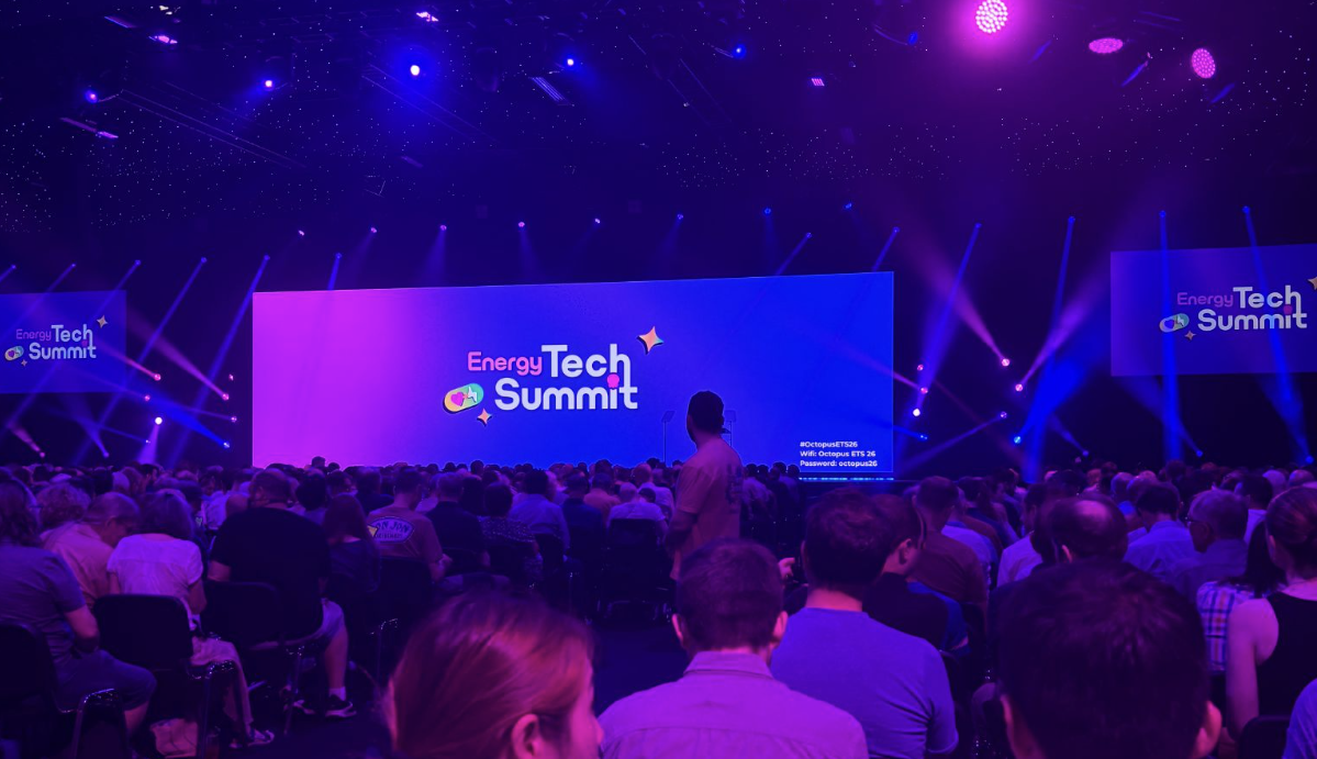 The main stage at the Octopus Energy Tech Summit during London Climate Action Week. A large audience is seated facing a brightly lit screen displaying the summit branding, with purple and blue stage lighting illuminating the conference hall.