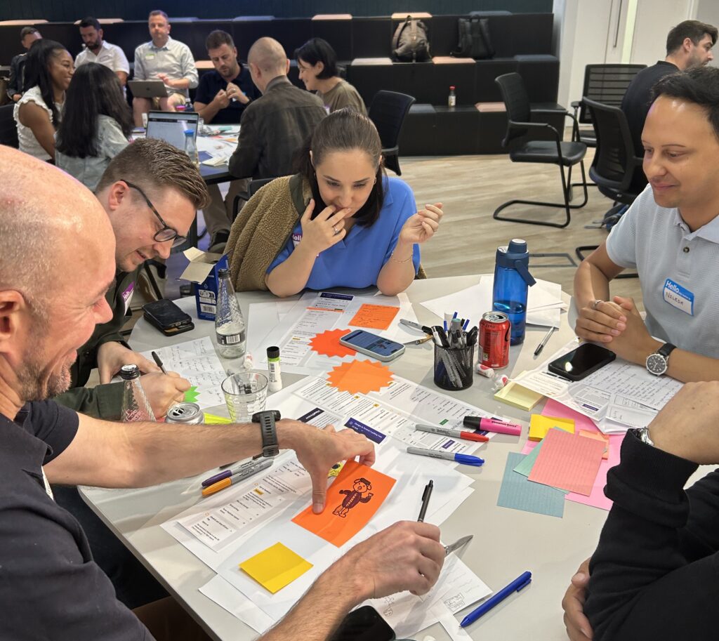 Attendees collaborate during Creative CX's Experimentation Day with Heathrow, using customer research, worksheets, sticky notes, and paper sketches to develop evidence-led solutions to a real customer challenge